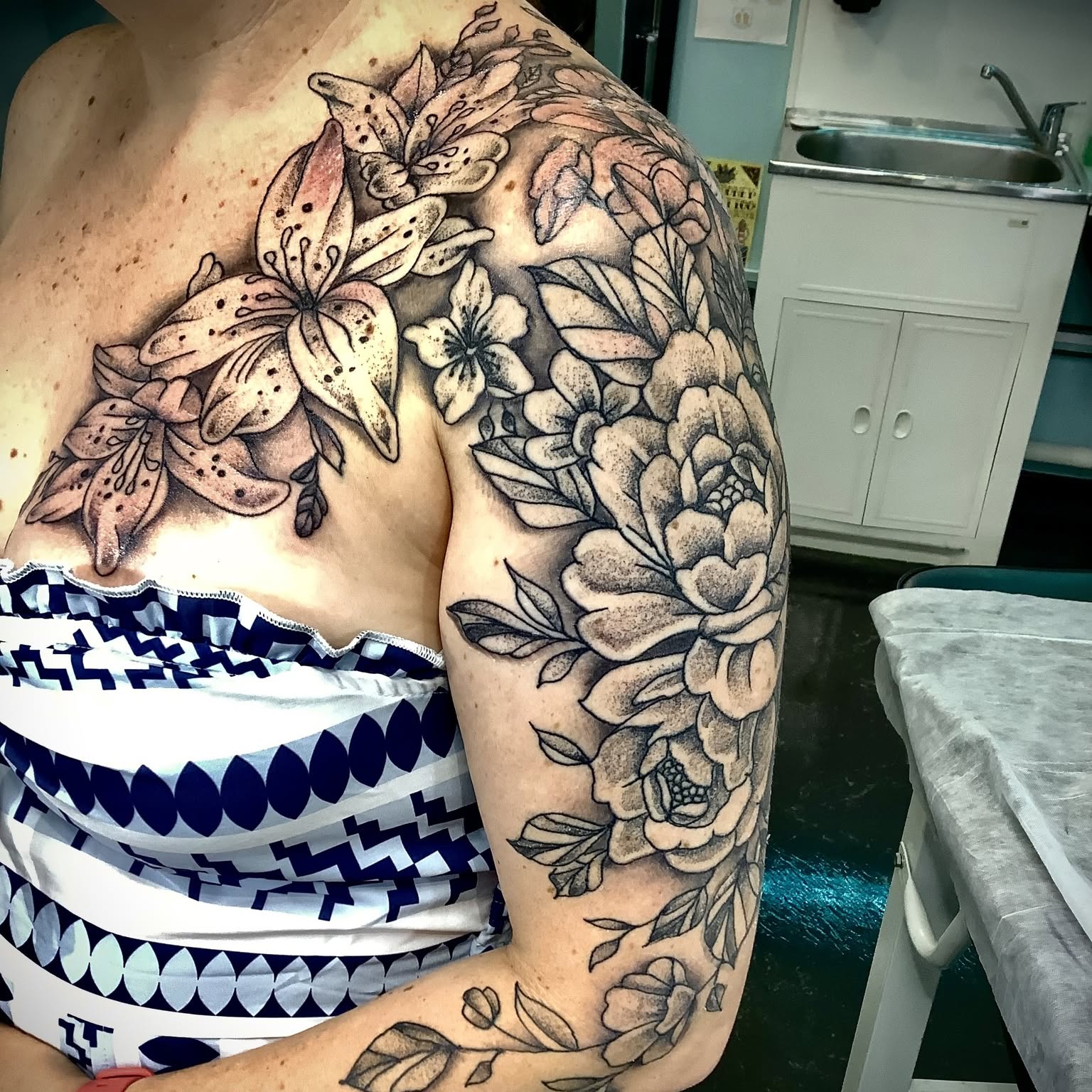 Black and grey lily and rose tattoo across the shoulder and upper arm