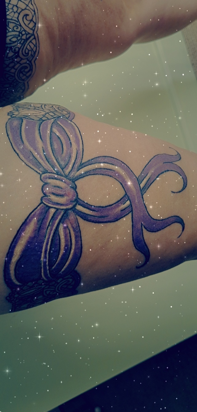 Purple ribbon bow tattoo on a thigh
